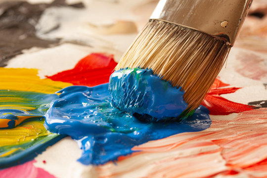 Close up of paintbrush picking blue color from an artist palette. Colorful image from an artist’s studio or a school showing creative education