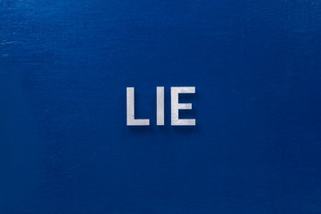 the word lies laid with silver metal letters on classic blue board in flat lay with central...