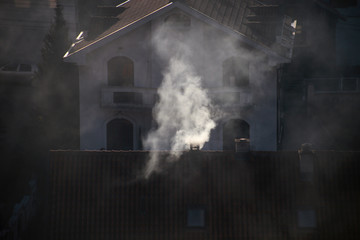 Smoking chimneys at roofs of houses emits smoke, smog at sunrise, pollutants enter atmosphere. Environmental disaster. Harmful emissions and exhaust gases into air. Fog, winter day, heating season.