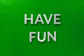 the words have fun laid with silver metal characters on green background in central flat lay...
