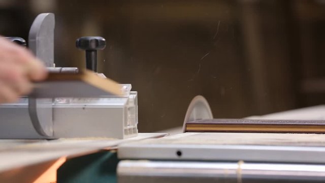 Close-up of carpentry machine with circular saw, sharp cutting blade cut wooden board in half, worker changes workpiece on machine and cuts it, sawdust fly, work in carpentry workshop, wood processing