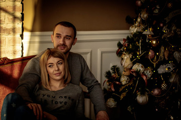 Fototapeta na wymiar Loving young couple spends Christmas at home near a decorated, festive Christmas tree. Man and woman are happy spending time together.