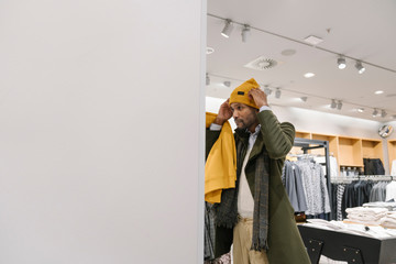 Stylish man shopping in a clothes store trying on a beanie