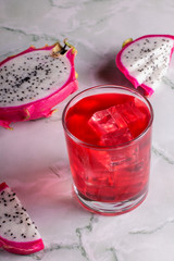 Glass of mango dragonfruit refresher drink on marble table with ice cubes. Copy space.