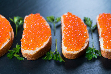 Sandwiches with red caviar on dark stone background