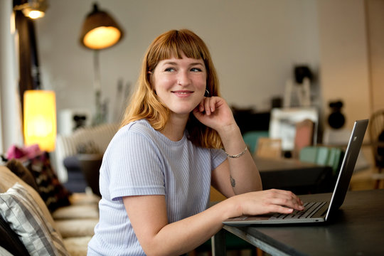 Portrait of strawberry blonde young woman with nose piercing using laptop in a coffee shop
