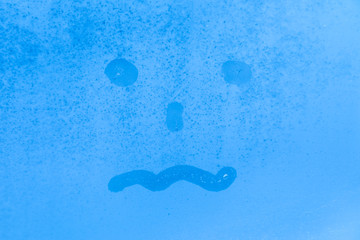 Fototapeta premium The picture or figure of the scared or tired face on the blue evening or morning window glass with drops 