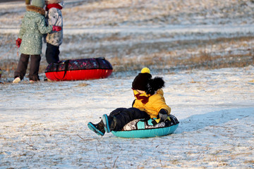 Fototapeta na wymiar Children having fun on snow tubes in a park, boy sliding down the hill. Winter entertainment, sledding and tubing in frosty day