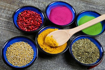 Close up view from above on six blue bowls with various colorful spice powder and grains on wood table. Spoon in turmeric curcuma bowl.