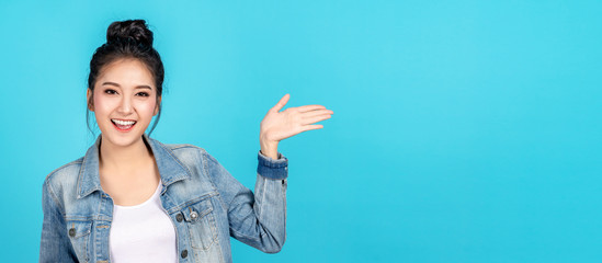 Banner of Happy asian woman feeling happiness and gesture hand open on blue background. Cute asia girl smiling wearing casual jeans shirt and present on copy space. © ChayTee