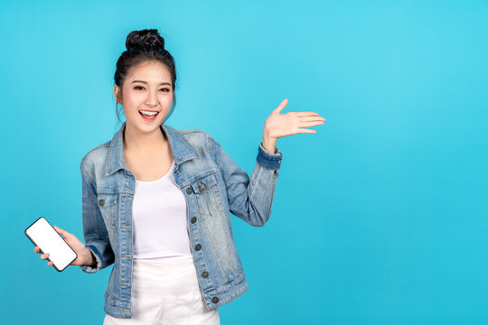 Happy asian woman feeling happiness and standing hold smartphone other hand open on blue background. Cute asia girl smiling wearing casual jeans shirt and connect internet shopping online and present