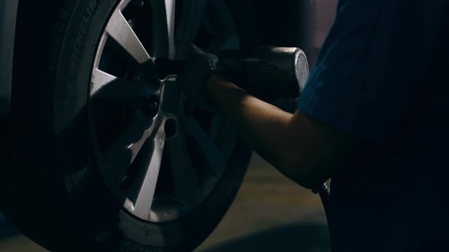 Professional car mechanic changing a car tire on lifted automobile at repair service station. Wheel alignment work at workshop night. Skillful Asian guy in uniform fixing car. 4k slow motion shot.