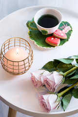 A candle with pink roses and cup of tea on white table