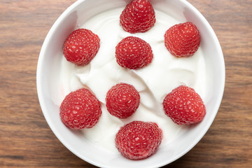 Cottage cheese with raspberries in a white bowl on a wooden table.
