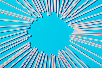Plastic cocktail straws scattered on a blue background, space for text in the center of the frame