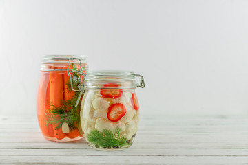 two glass jars of fermented cauliflower, carrots. vegetables on a light background. fermentation is a source of probiotic