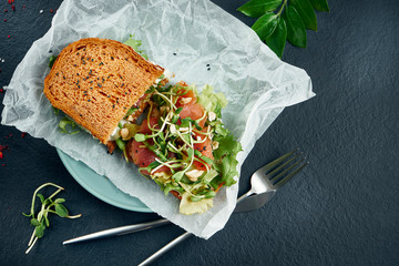 Trendy street snack. Tasty sandwich toast with salmon and microgreen on craft paper on a black...