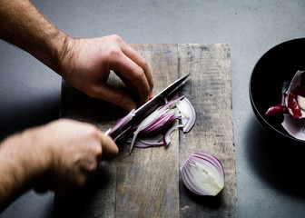 Overhead view of man's hands cutting onion on cutting board