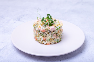 Olivier salad on a white plate, decorated with pea sprouts. Traditional New Year and Christmas Russian salad. Close-up, selective focus.