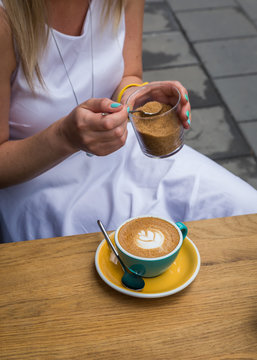 Midsection of woman adding brown sugar to latte coffee