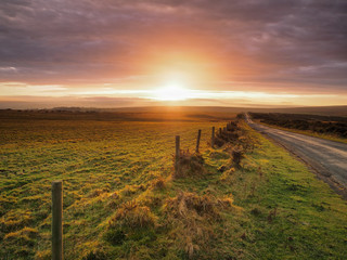 Beautiful sunset lighting up the clouds over Danby Moor with road and fence leading off into the...
