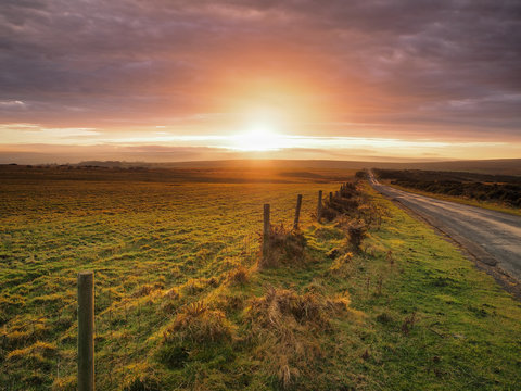 Beautiful sunset lighting up the clouds over Danby Moor with road and fence leading off into the distance, North York Moors National Park, UK