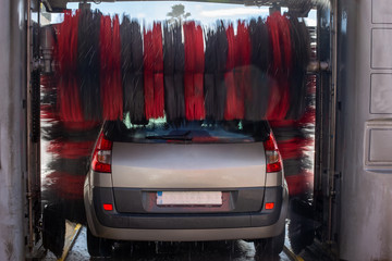 Back view of a car wash cleaning a car with rotating brushes.