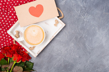 Valentine's Day concept. Morning coffee, envelope with red heart, roses on grey desk. Free space. Space for text. 