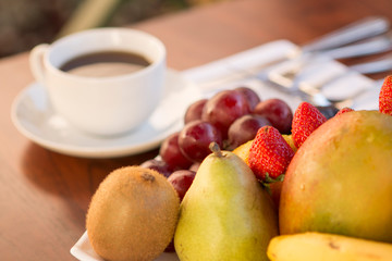 Colorful various fruits with white cup of coffee in the back over a wood table with natural light