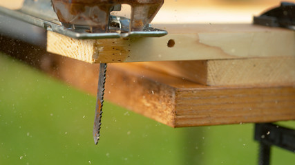 MACRO: Jigsaw blade cuts into plywood plank sitting on the carpenter's workbench