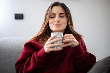 Young woman having a hot drink witting on her sofa