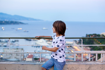 Preschool child, boy, sitting on a fence on the top of Monaco, enjoying the view in the arly...