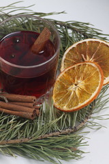glass of mulled wine, cinnamon sticks and orange chips with fir bough on white background. Vertical image