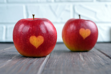 Two red apples with a heart seal on the table. Orange heart on organically grown fruits. Growing fruits with prints.