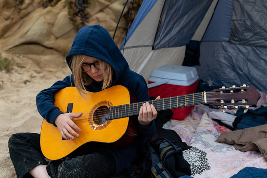 Tween sitting playing guitar in front of tent on beach