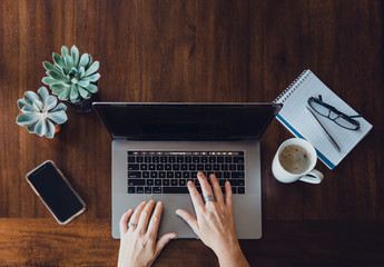 Overhead view of woman's hands working on laptop at wooden table.