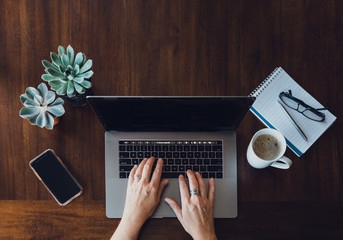 Overhead view of woman's hands working on laptop at wooden table.