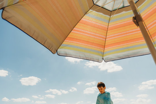 View from under parasol of boy wrapped in towel against blue sky