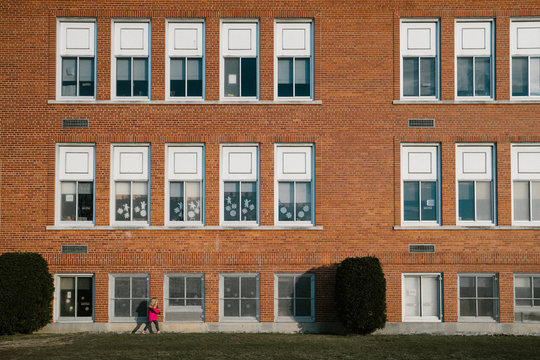 A little girl in a pink coat walks past a school building.