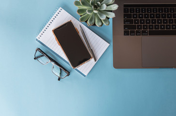 Overhead view of workspace with laptop, phone, glasses and notepad.