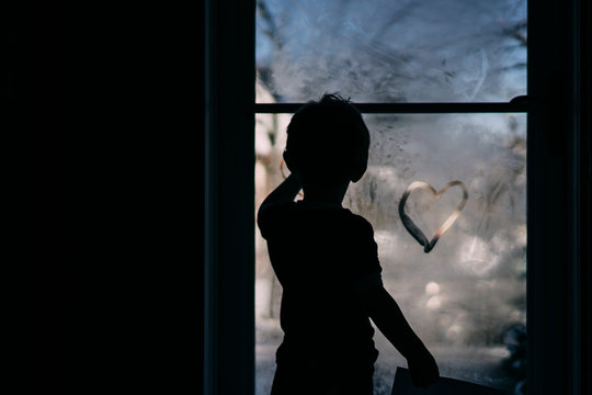 A little boy draws a heart on a foggy storm door.