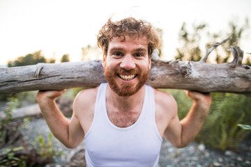 portrait of man balancing log on shoulders during an outdoor workout.