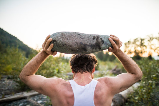 rear view of man lifting rock above head during an outdoor workout.