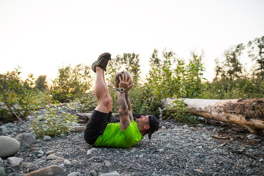 side view of fit man using a large rock in his workout.