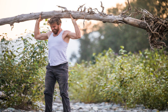 Muscular man completes a standing overhead press using a tree.