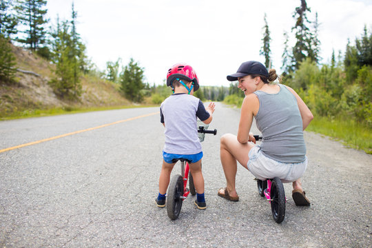 Mother biking and laughing with son on a small balance bike.