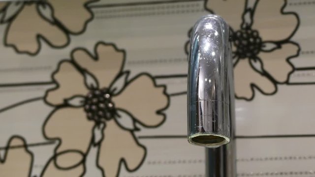 a close-up on a dripping tap in the bathroom. In the background there are tiles with a floral pattern.  concept of environmental protection and money saving