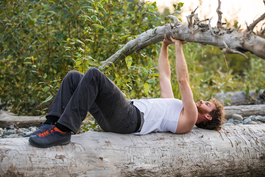 Side view man bench pressing a fallen tree during an outdoor workout.
