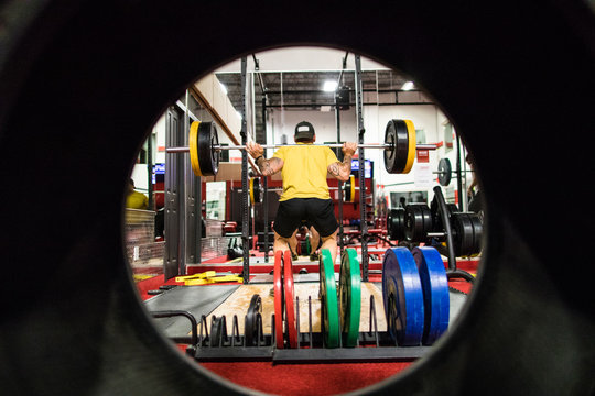 View through tire of muscular man doing squats at the gym