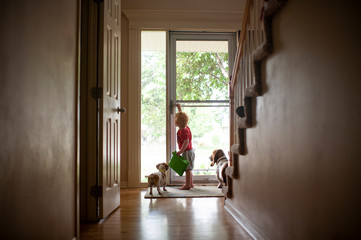Young boy opening the front door for dogs at home while holding tablet